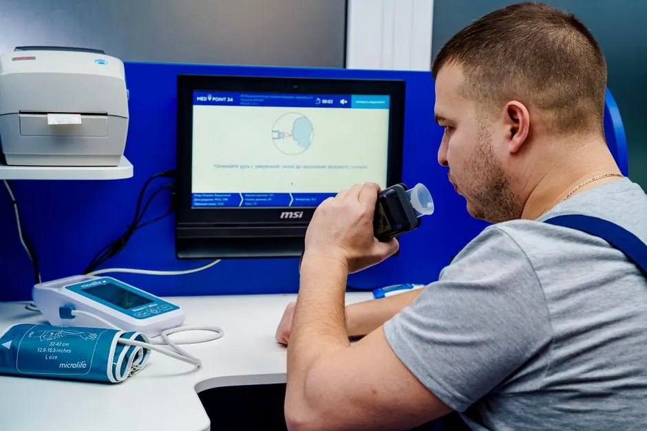 A man uses a breathalyzer device in a medical facility during the day.