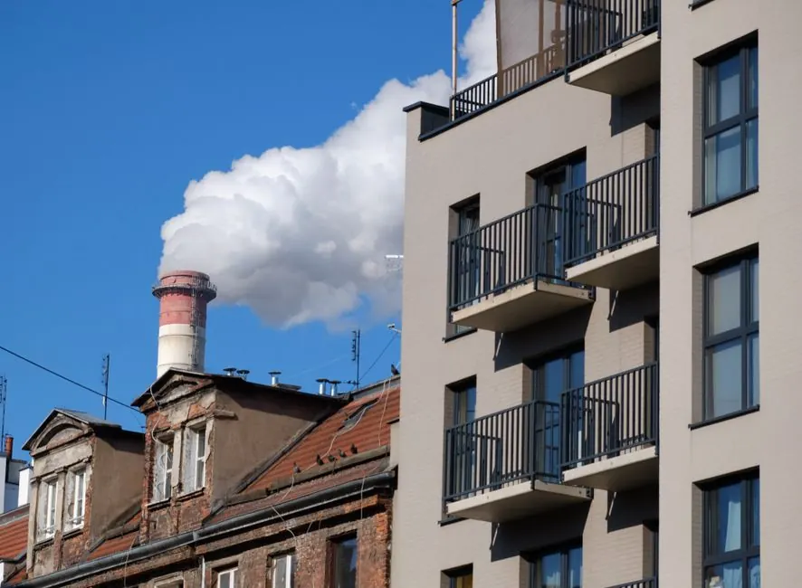 Urban skyline with modern and old buildings, contrasting industrial smokestack.